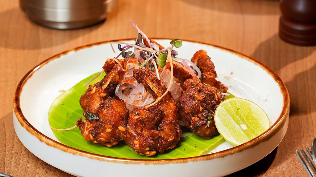 Fried seafood on a banana leaf, topped with sliced onion and microgreens, with a wedge of lime