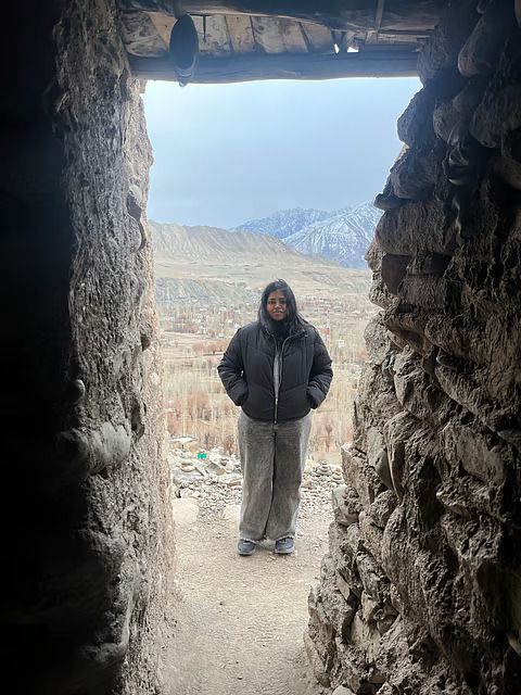 Shivani Illakiya standing in a stone doorway, with snow-capped mountains behind her